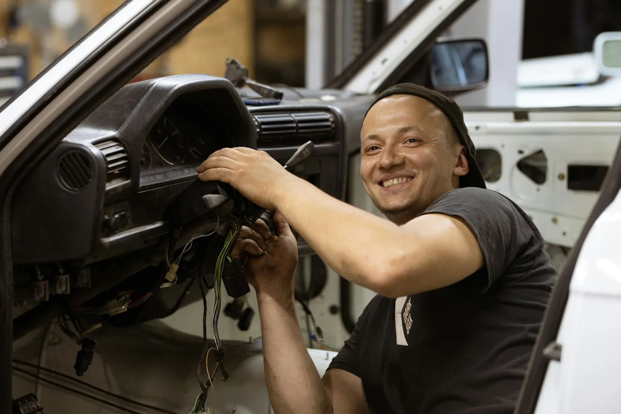 Smiling mechanic working on a vehicle's dashboard wiring