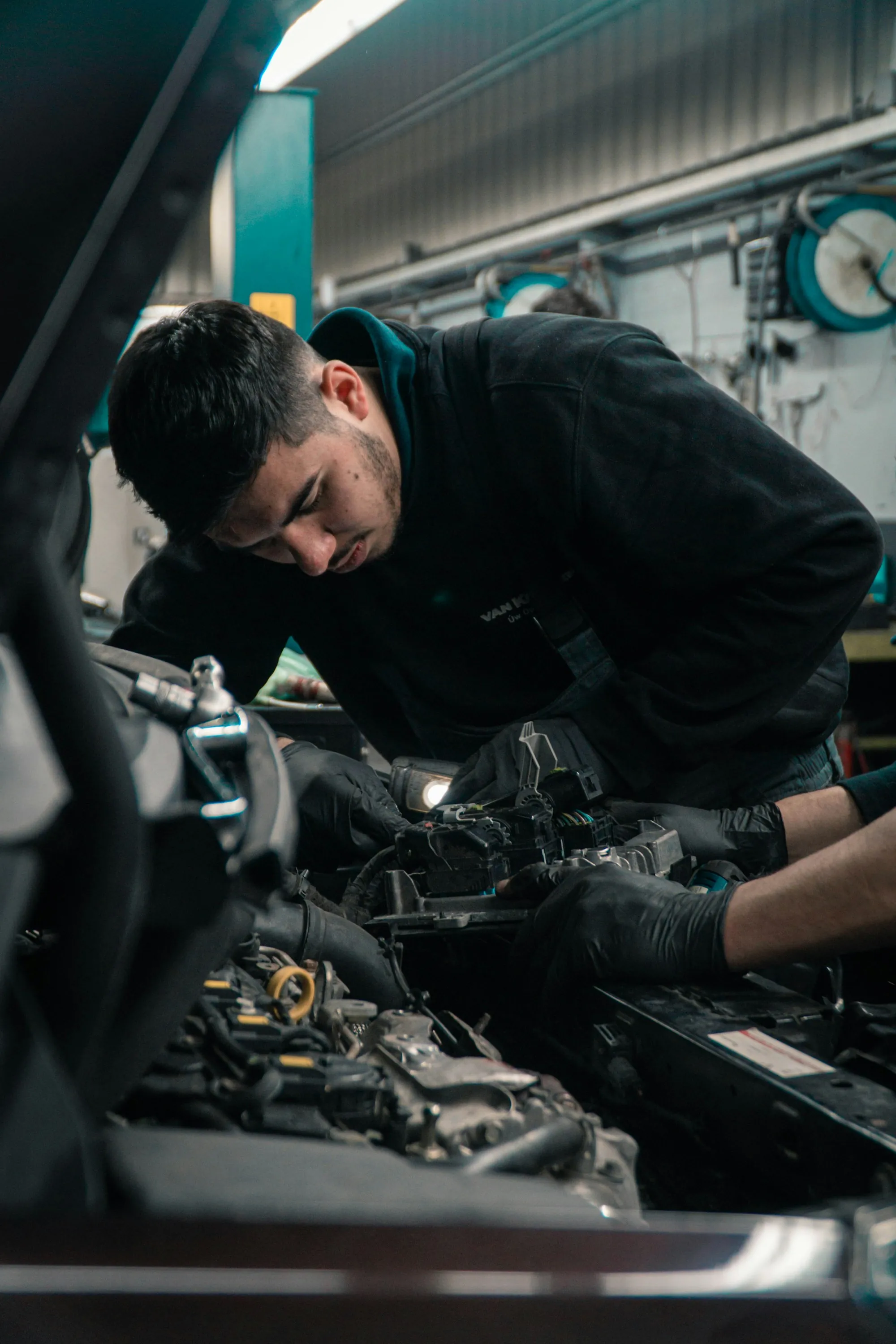 Technician working inside a car's engine bay under shop lights