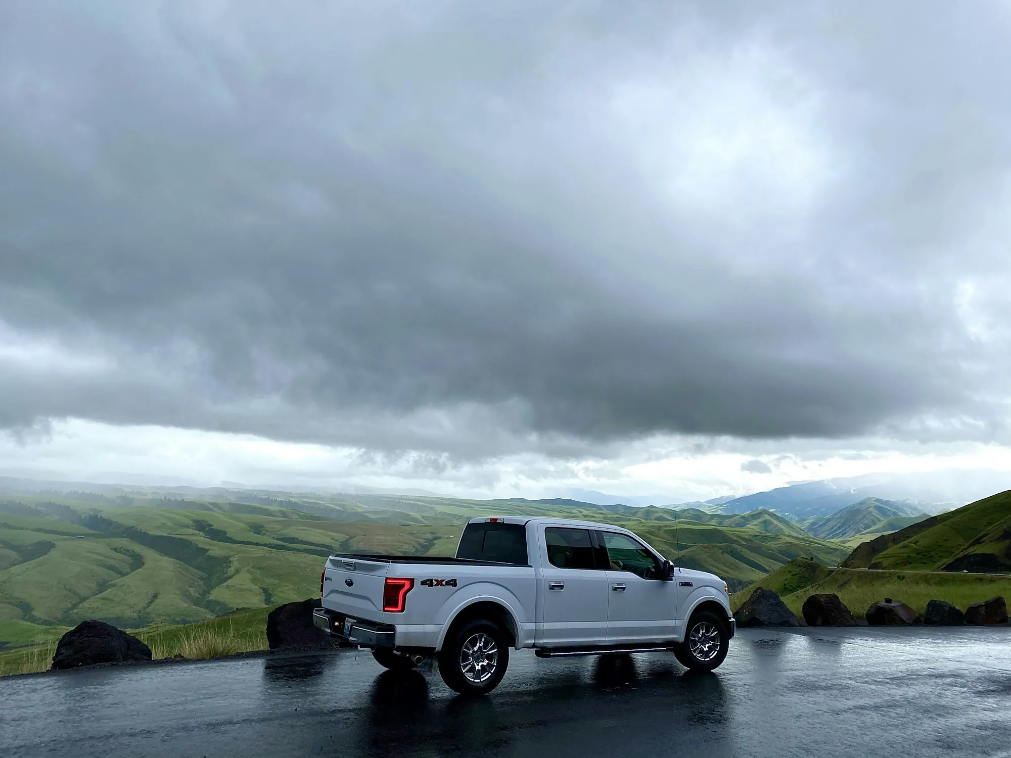 White pickup parked on a road with green hills under a cloudy sky