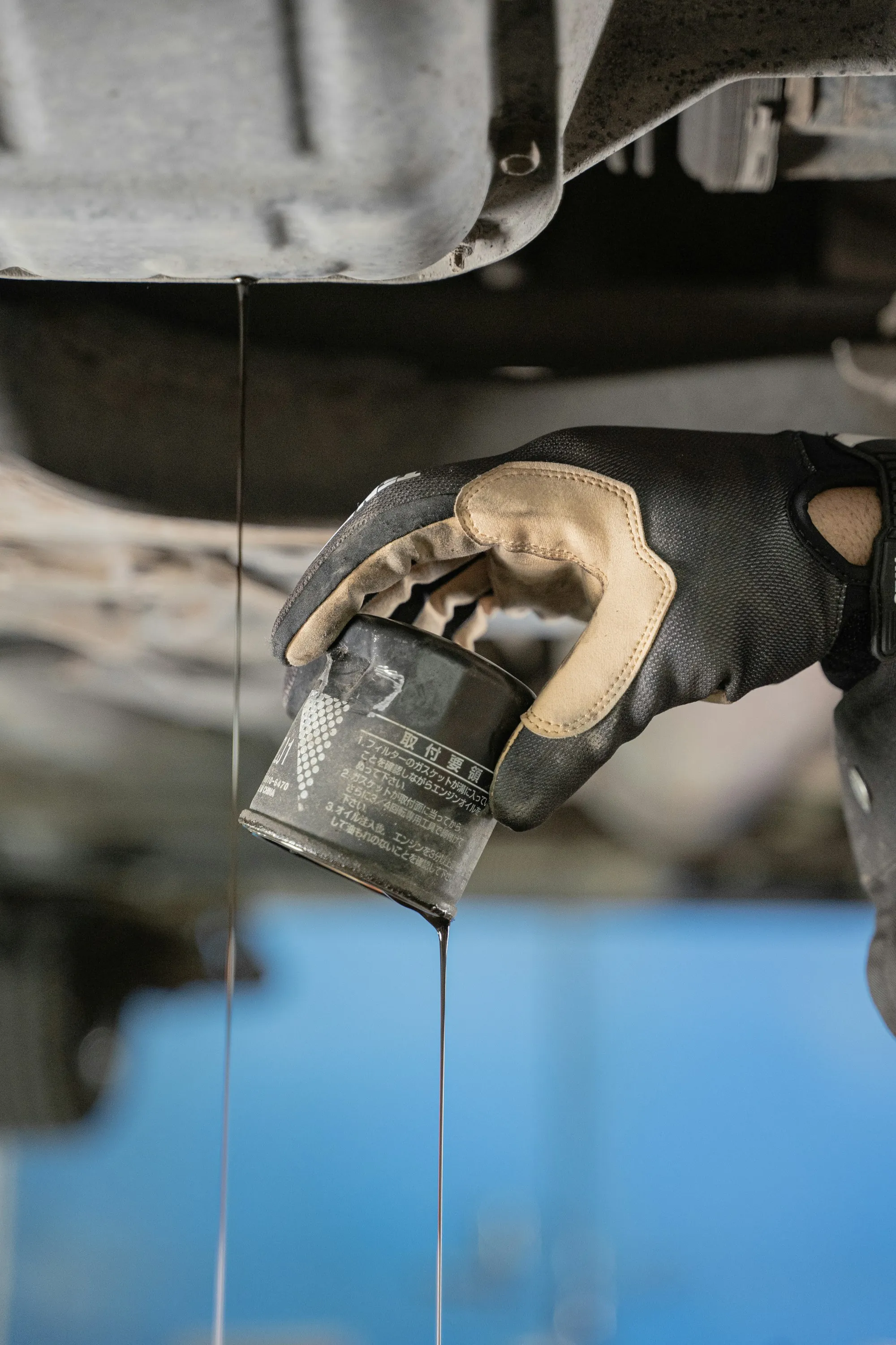 Gloved hand draining an oil filter under a vehicle