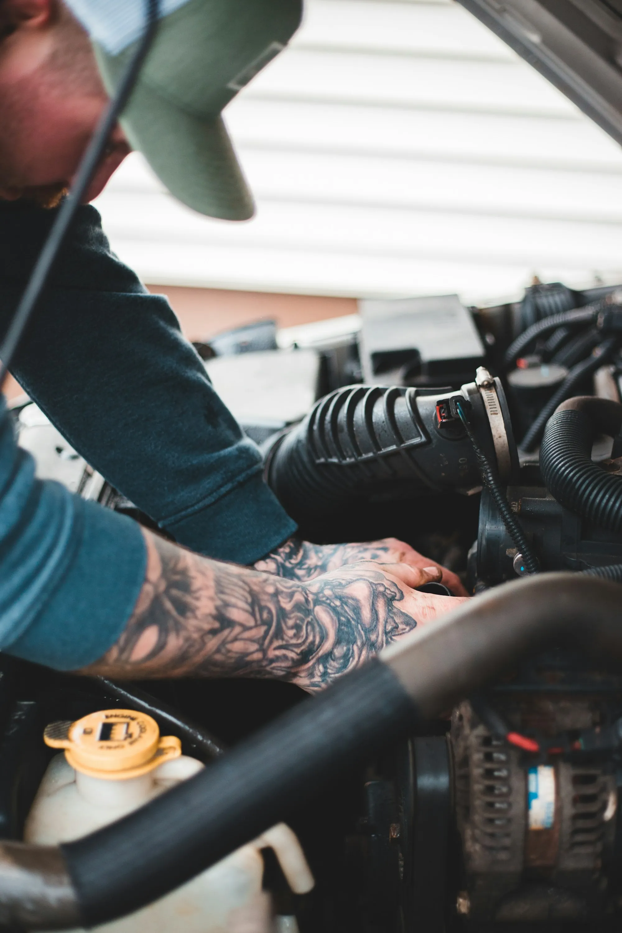 Tattooed forearms of a mechanic tightening a part in an engine bay