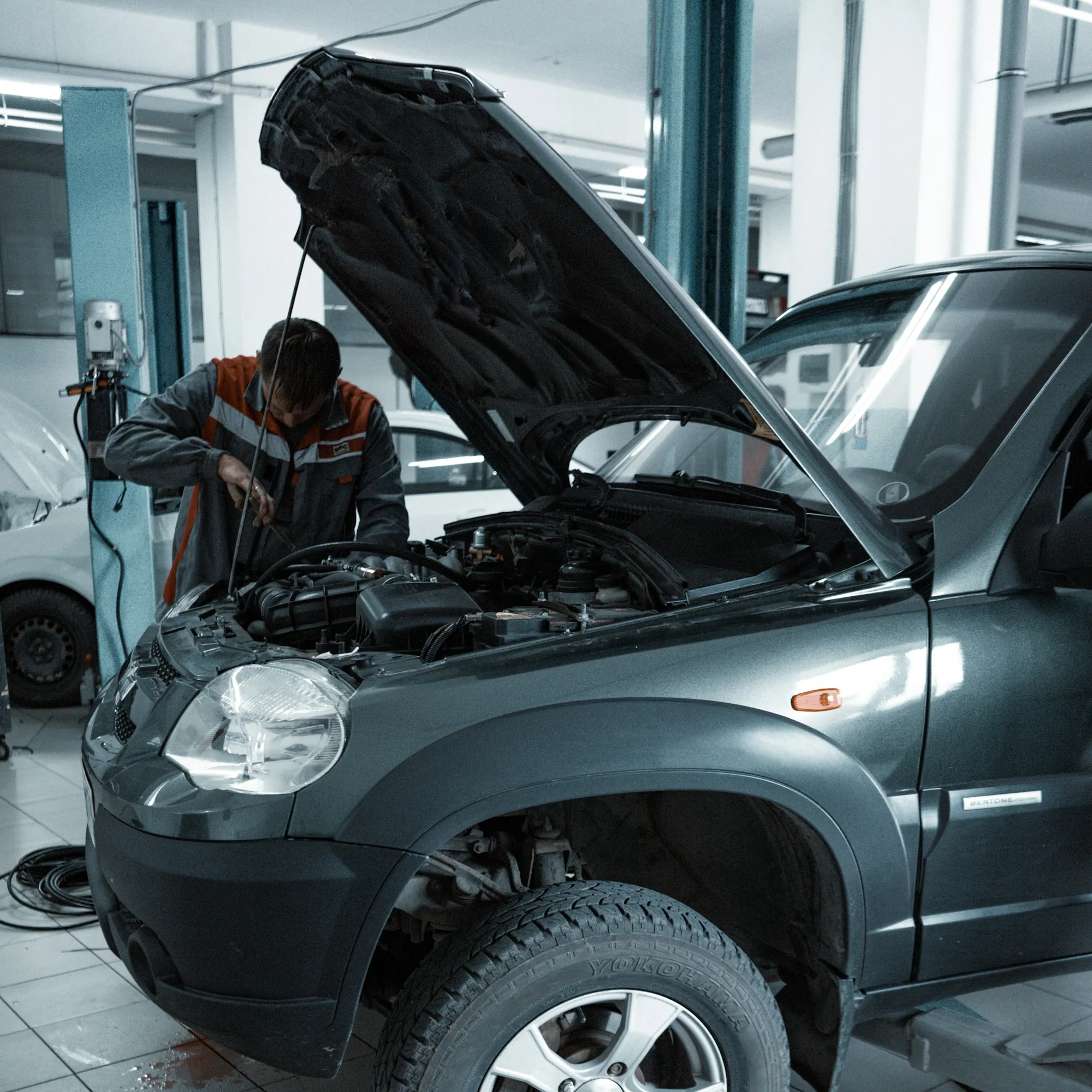 Mechanic reaching into the engine bay of a grey SUV with the hood raised